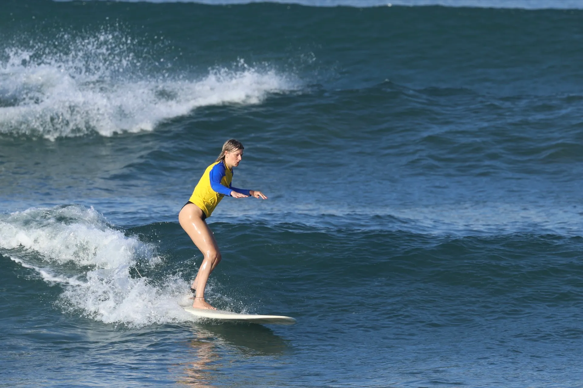 A beginner surfer balancing on a gentle green wave during a Canggu lesson