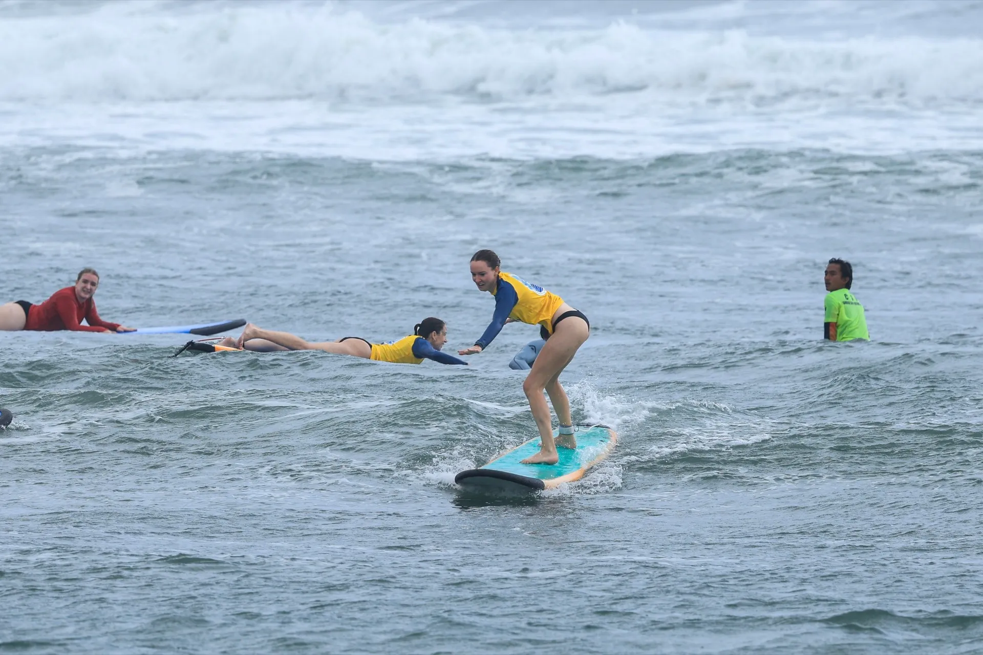 A beginner standing on a soft-top board while an instructor watches nearby at Batu Bolong